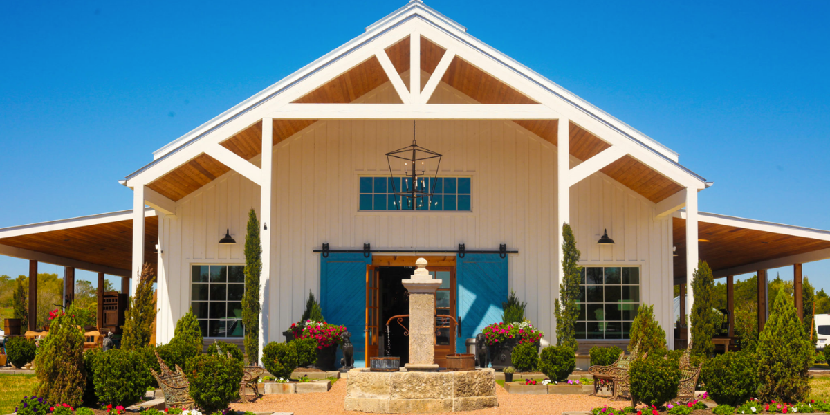 Entrance to an antique barn at The Compound in Round Top, Texas, with a white gabled roof, hanging chandelier, and a fountain in the courtyard
