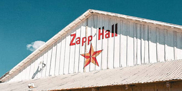 The white exterior of Zapp Hall Antique Show in Warrenton Texas with the hand-painted Zapp Hall name and red star logo against a blue sky