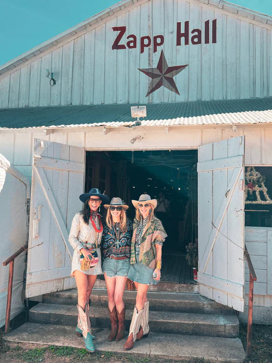 Three women posing on the steps of the Zapp Hall building with the hand-painted Zapp Hall sign and red star visible on the metal siding behind them