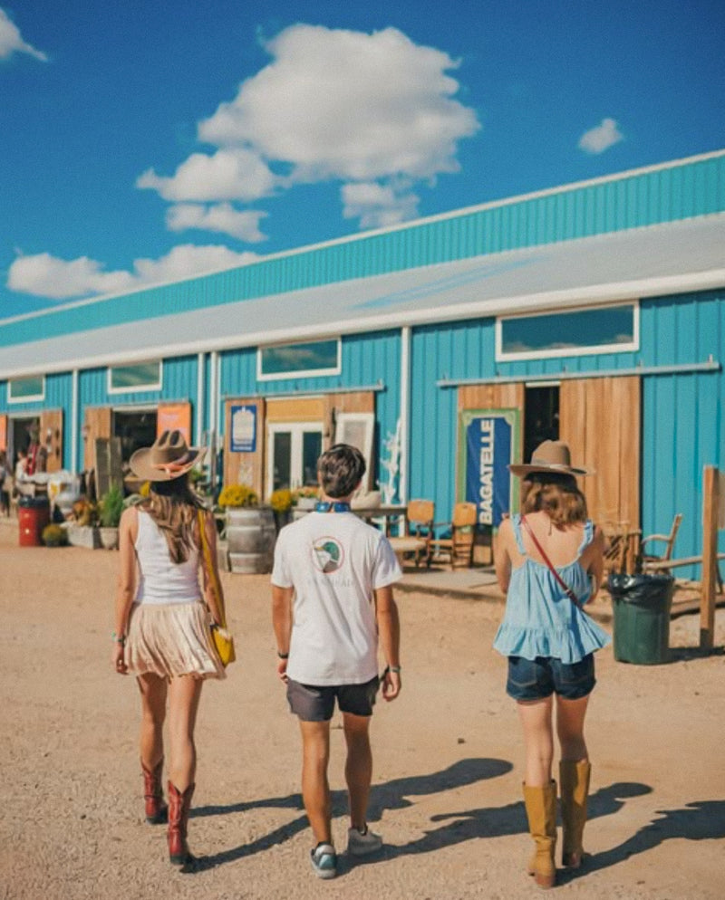 Three shoppers walking toward the bright blue barns at Blue Hills antique venue in Round Top, Texas