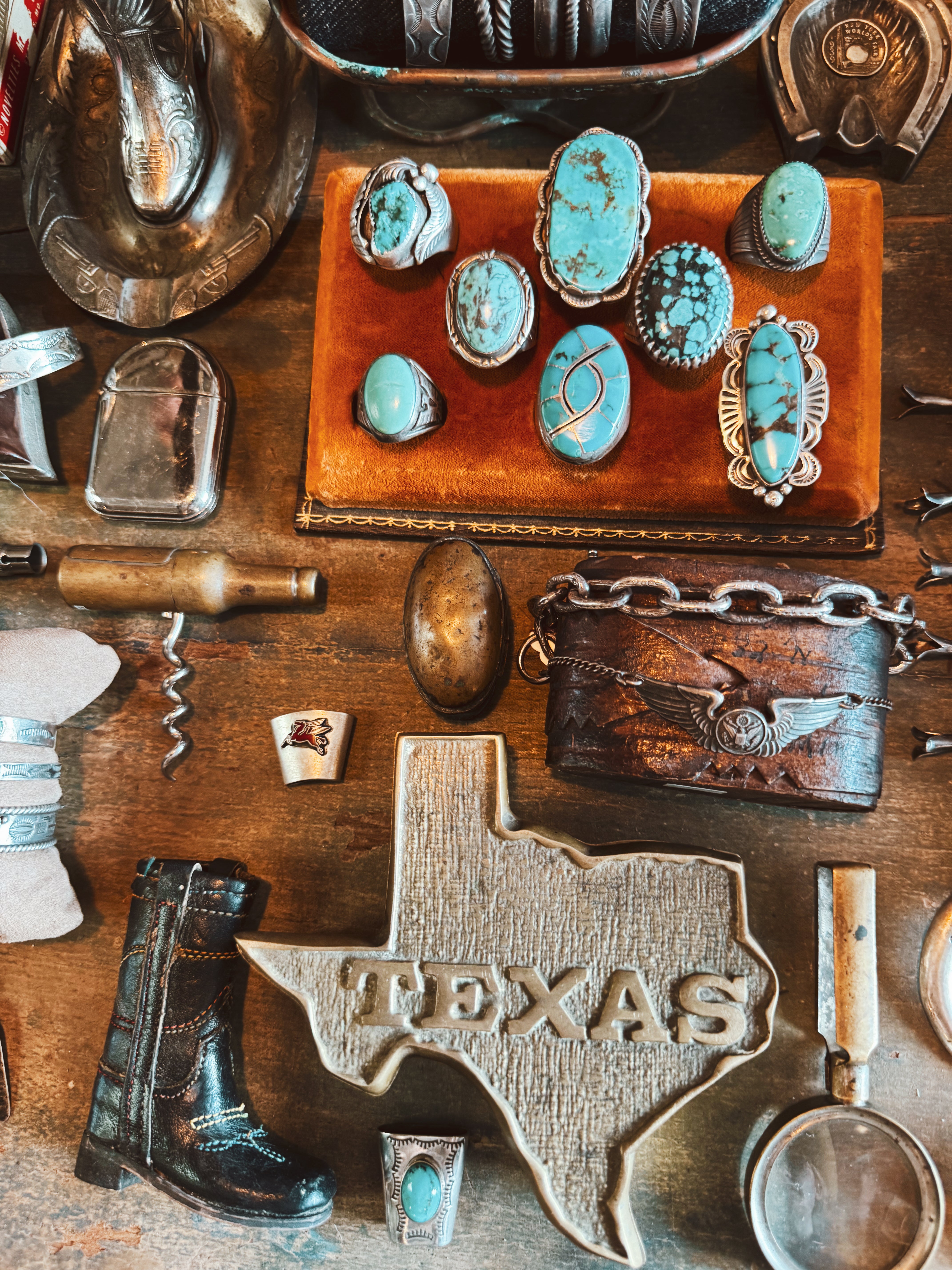 Turquoise rings, vintage brooches, a wooden Texas cutout, and antique collectibles displayed on a leather surface at the Round Top antique show